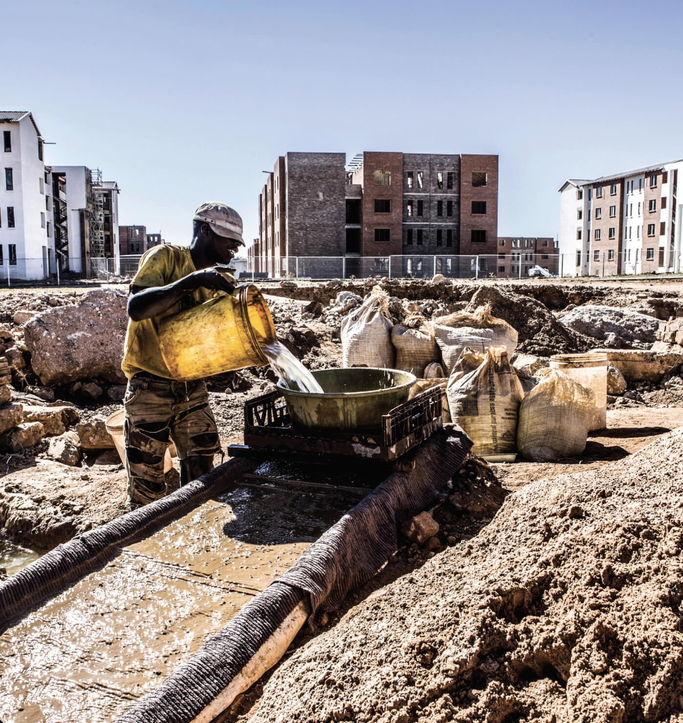 Parallel worlds. An informal miner washes gold on a construction site alongside a housing development in Fleurhof, which runs along Main Reef Road to the west of the city centre.